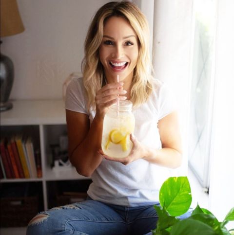 Clare Crawley in a white t-shirt and blonde hair poses a picture while having a refreshment drink.